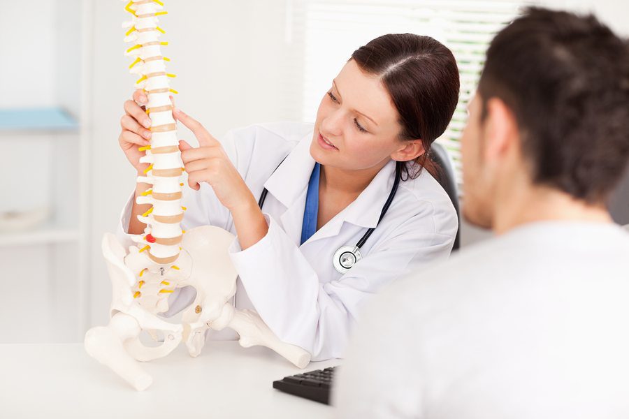 Doctor holding a spine model and explaining vertebrae to a patient during a consultation.