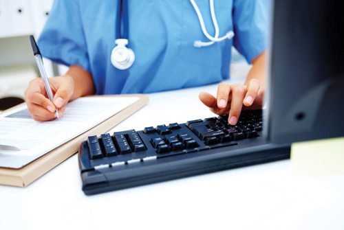Nurse or clinician entering patient information on a computer and writing on a medical form.