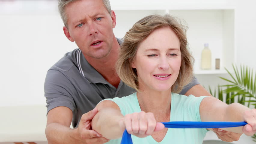 Rehabilitation specialist assisting woman with shoulder therapy using a resistance band