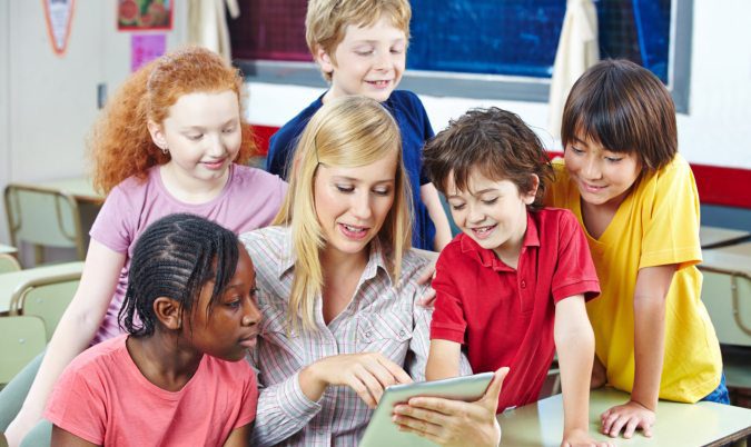 Speech therapist working with group of children using digital tablet in classroom.
