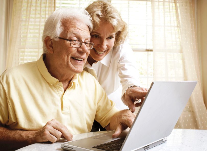 Smiling senior couple using a laptop together at home near a bright window.