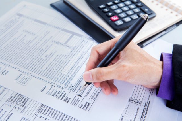 Person reviewing financial documents and calculating accounts receivable using a calculator.