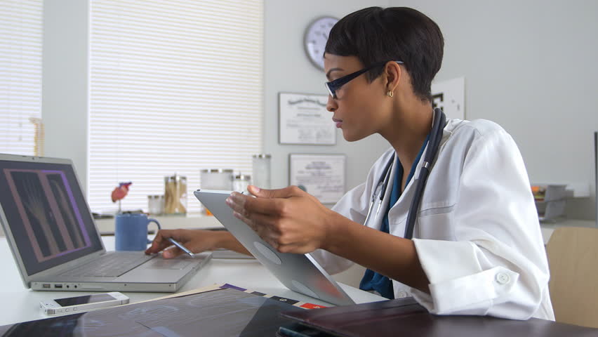 Physician wearing a lab coat and stethoscope using digital tools to manage patient information.