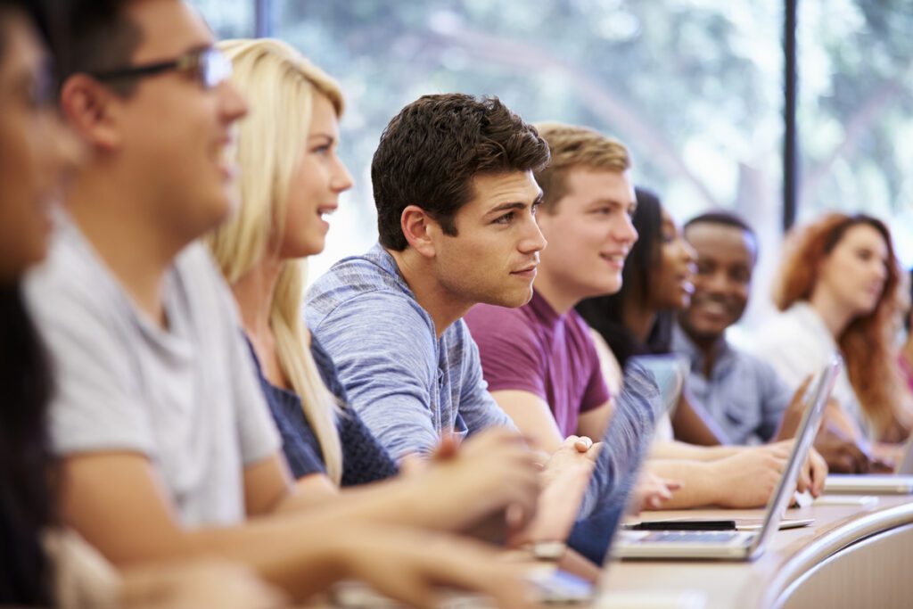 Group of young adults learning in a modern classroom environment with laptops.