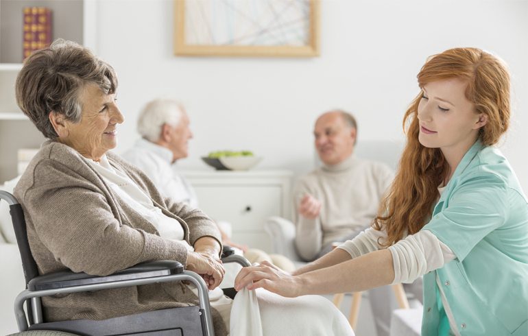 Caregiver assisting elderly woman in wheelchair during rehabilitation session.