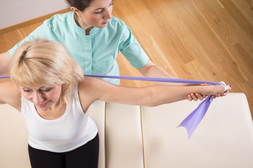 Physiotherapist helping woman perform shoulder exercise with resistance band.