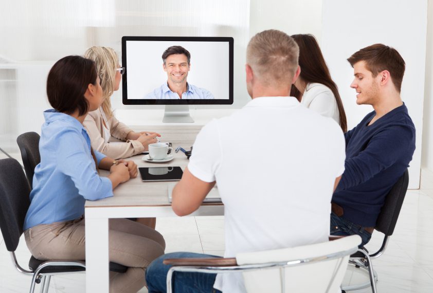 Team attending virtual meeting with presenter on video conference screen.