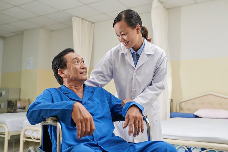 Doctor supporting senior patient in wheelchair during recovery at hospital.