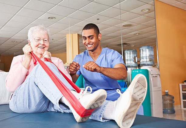 Physiotherapist assisting elderly woman with resistance band exercise in clinic.