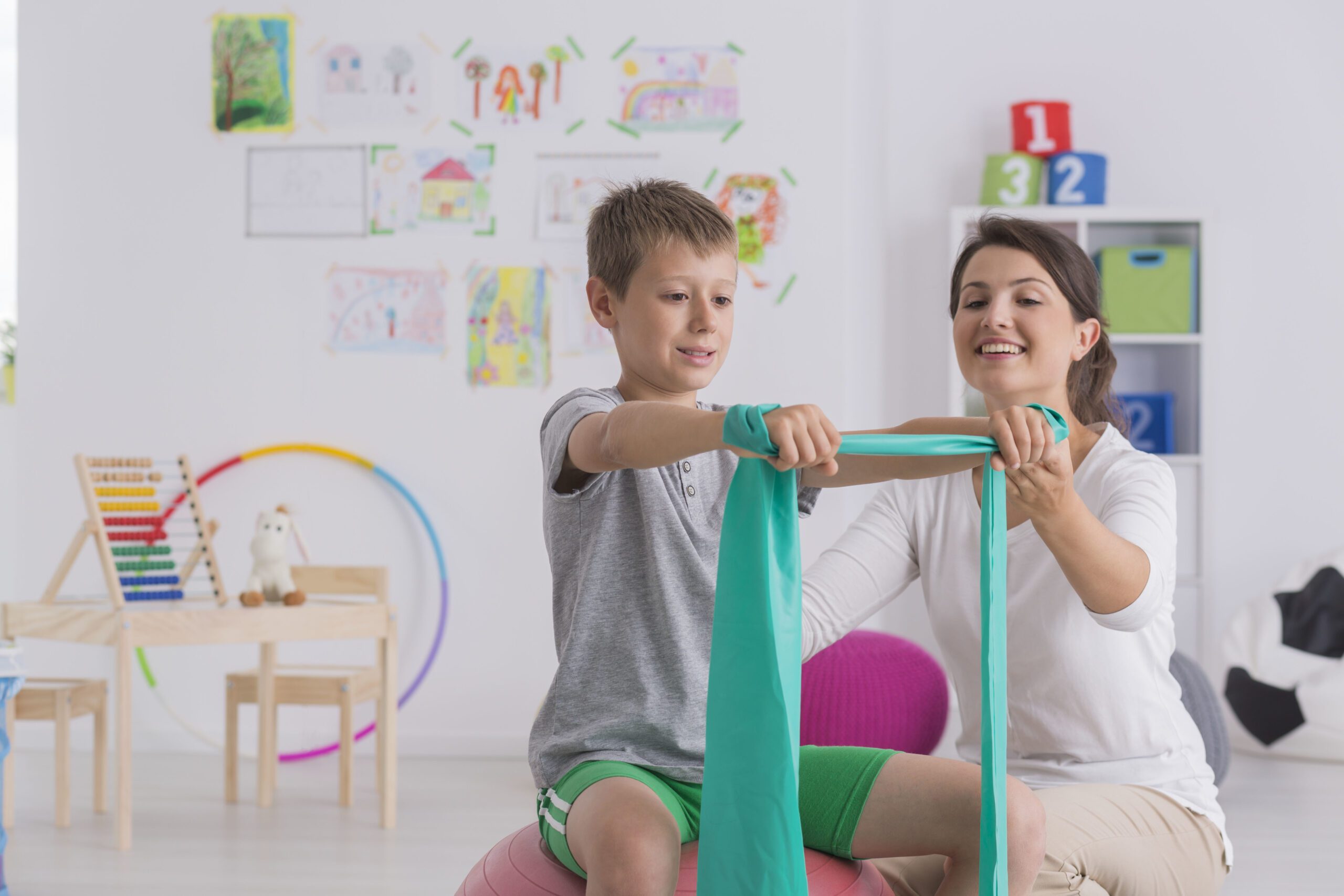 Pediatric occupational therapist helping a child with resistance band exercises in a colourful therapy room.