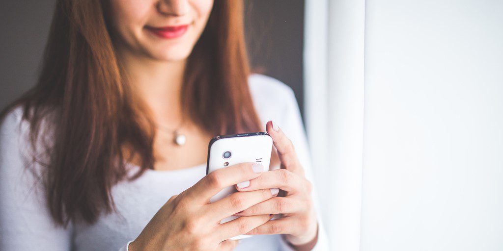 Smiling physical therapist using smartphone to communicate with patients.