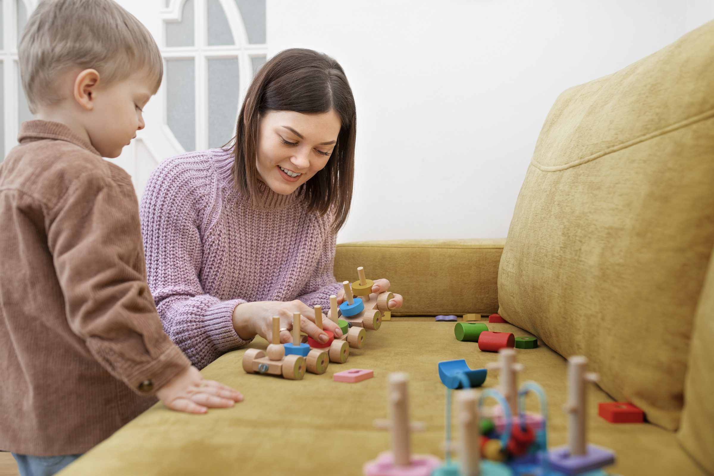 Woman helps toddler build with colourful wooden blocks and stacking toys during playtime.
