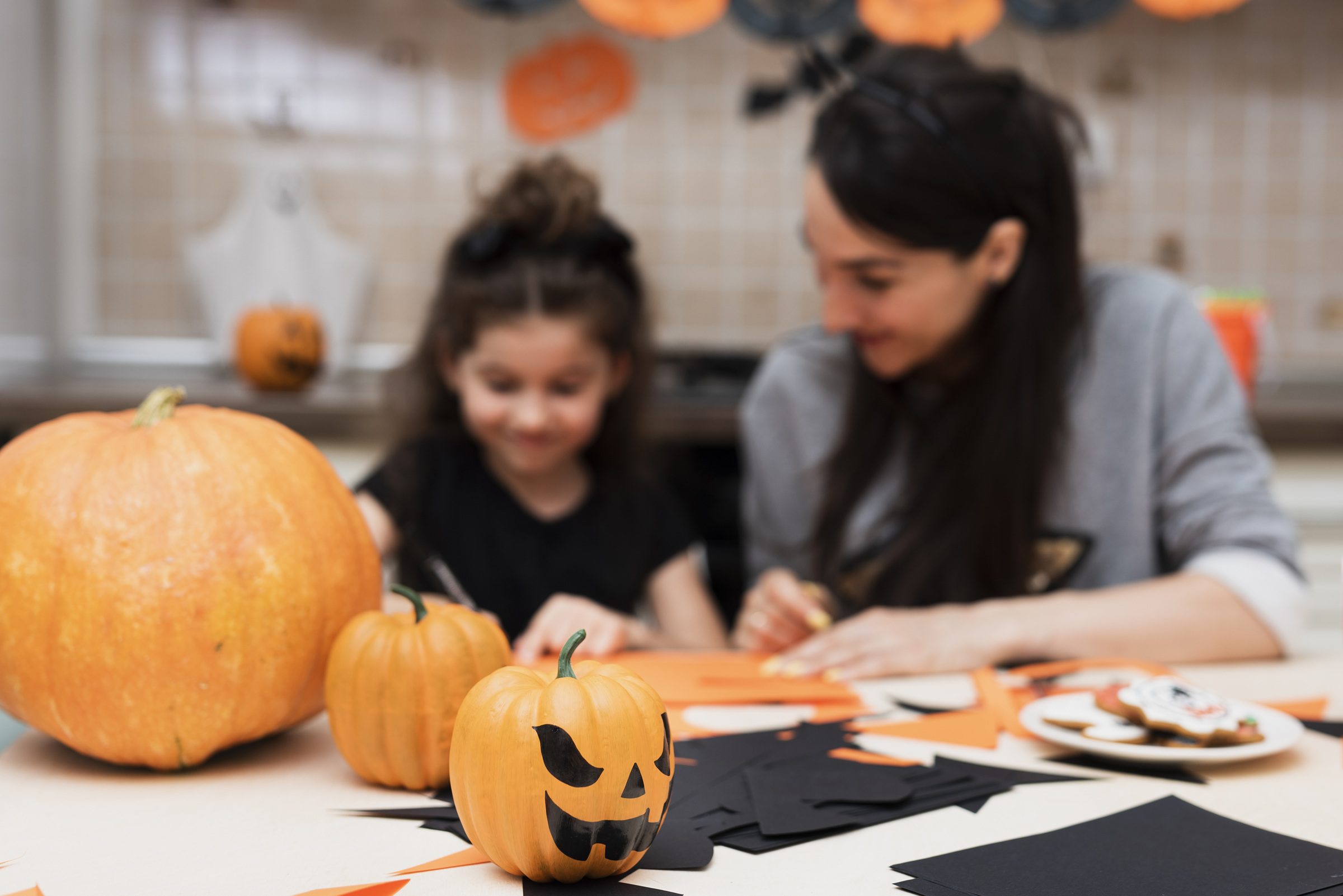 Parent and daughter crafting Halloween décor with pumpkins and black paper at home.